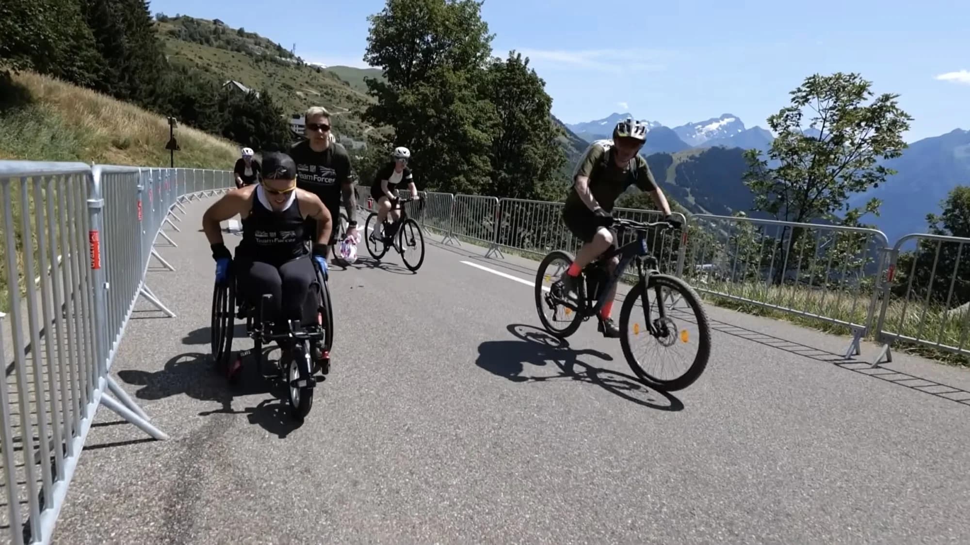 Lexi pushing her standard wheelchair up Alpe d'Huez, with Team Forces cyclists alongside